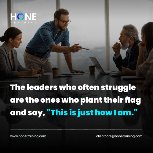Leader stands and points to a team seated around a conference table in a glass-walled room; quote overlay reads 'This is just how I am.'